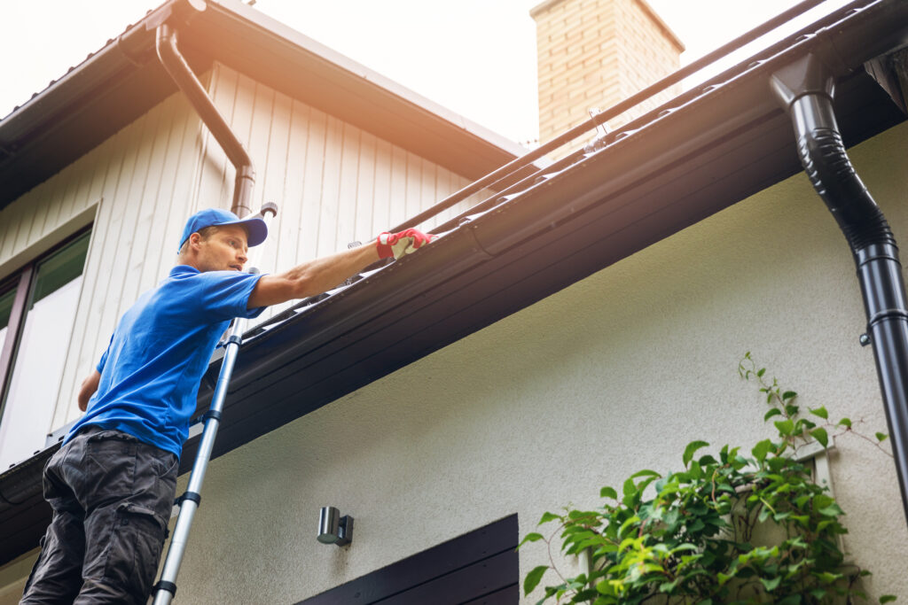 Man on a ladder cleaning leaves out of a gutter